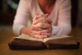 Unrecognizable woman praying, hands clasped together on her Bibl