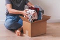 Unrecognizable woman putting clothes in cardboard box while sitting on the floor. Royalty Free Stock Photo