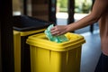 Unrecognizable woman recycling plastic in yellow garbage can