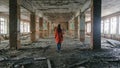 Unrecognizable woman in a red cloak inspects destroyed building after the disaster earthquake, flood, fire.