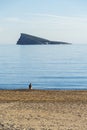 Unrecognizable woman in Santa hat sitting alone in empty beach with Mediterranean sea and Benidorm island background Royalty Free Stock Photo