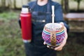 unrecognizable woman serving mate with a red thermo, in a colorful ethnic mate.