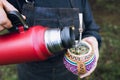 unrecognizable woman serving mate with a red thermo, in a colorful ethnic mate.