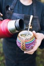 unrecognizable woman serving mate with a red thermo, in a colorful ethnic mate. Vertical