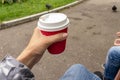 Unrecognizable woman sitting on a bench in park with her family and holading a red paper takeaway cup of hot coffee in