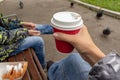 Unrecognizable woman sitting on a bench in park with her family and holading a red paper takeaway cup of hot coffee in her hand,