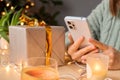 Unrecognizable woman using smartphone doing online shopping buying presents for Christmas holidays sitting at table with gift box Royalty Free Stock Photo