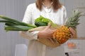 Unrecognizable woman wearing white shirt preparing to cook lunch holding avocado pineapple leek green lettuce leaves in light