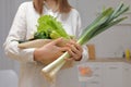 Unrecognizable woman wearing white shirt preparing to cook lunch holding zucchini cucumber leek green lettuce leaves in light