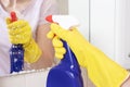 Unrecognizable woman in yellow rubber gloves holding a blue cleaning spray bottle and sprinkle on a glass mirror surface. Washing Royalty Free Stock Photo