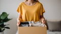 Unrecognizable woman in yellow t-shirt holding box with clothes. Clothing donation.