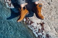 Unrecognizable woman in yellow trekking boots sits on coast near of turquoise water, top view. Adventure, scout, discovery, explor