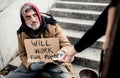 Unrecognizable woman giving money to homeless beggar man sitting in city.