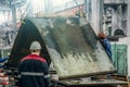 Unrecognizable workers at metallurgical plant unload steel or metal sheets with crane