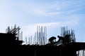 unrecognizable workers are working at construction site with many vertical rebars building a structure in front of blue