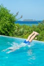 boy diving in the turquoise water of a swimming pool. a wonderful tropical island in the background Royalty Free Stock Photo