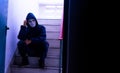 Unrecognizable young man white mask and hoodie sitting on old stairs,. Sadness, despair, dark, concept