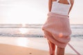 Unrecognizable young slender female stand alone on the beach or ocean at sunset and look at water. Woman dressed in a