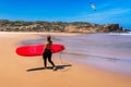 Unrecognizable young woman carrying surf board at Praia da Bordeira, Portugal. Young woman holding surf board on the sea shore.