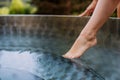 Unrecognizable young woman is dipping her foot in outdoor hot tub,trying temperature of water, spa, beauty and Royalty Free Stock Photo