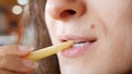 Unrecognizable young woman is eating french fries in fast food restaurant. She is holding one hand potato, mouth closeup