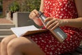Unrecognizable Young woman in red dress drinking water from metal bottle Writing Gratitude Journal on wooden bench