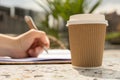 Unrecognizable Young woman study in beach resort. Drinking coffee from paper cup. Student making homework Female hands Royalty Free Stock Photo