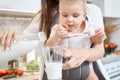 Unrecognized caring woman with kid is pouring milk into the glass in the kitchen Royalty Free Stock Photo