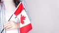 Unrecognized girl student in white blue shirt holding small canadian flag over gray background, Canada day, holiday, vote,