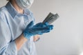 An unrecognized man in a white shirt holding a dollar, shows a surprised gesture. Wearing a medical mask and latex