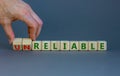 Unreliable or reliable symbol. Businessman turns wooden cubes and changes the word unreliable to reliable. Beautiful grey Royalty Free Stock Photo