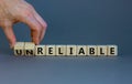 Unreliable or reliable symbol. Businessman turns wooden cubes and changes the word unreliable to reliable. Beautiful grey Royalty Free Stock Photo