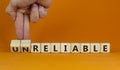 Unreliable or reliable symbol. Businessman turns wooden cubes and changes the word unreliable to reliable. Beautiful orange Royalty Free Stock Photo