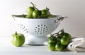 Unripe green tomatoes in colander and on table in white wooden kitchen background Royalty Free Stock Photo