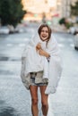 Unruly woman wrapped in blanket drinking coffee in the middle of empty city road