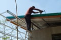 Unsafe Male Roofer Workman Using Electric Screwdriver Install Tile on Roof of New House in the Construction Site