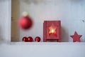 Unsharp red christmas ball at a branch in front of a shelf with red christmas decoration, star, lantern with candle light Royalty Free Stock Photo