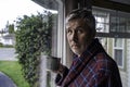 Unshaved middle aged man with messy hair holds coffee by window