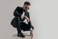 Unshaved young groom in black tuxedo crouching on wooden box Royalty Free Stock Photo