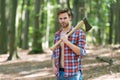 Unshaven handsome man in open plaid shirt with jeans carry large splitting axe in summer forest natural landscape Royalty Free Stock Photo