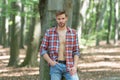 Unshaven lumbersexual man in unbuttoned lumberjack shirt standing at tree forest background Royalty Free Stock Photo