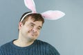 Unshaven man with bunny ears on a gray background. Faddish man is smiling.