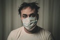 Unshaven man in a medical mask with tousled hair looking at the camera. On white background. Image toned in gloomy tones. dark,