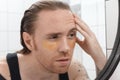 Unshaven man with patches under his eyes looks at himself in the bathroom mirror. Male with morning hangover Royalty Free Stock Photo