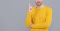 Unshaven man in yellow sweater cropped view keep raised finger grey background copy space, eureka