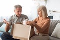 Displeased Senior Couple Unpacking Cardboard Box At Home