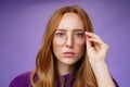Unsure and serious-looking focused redhead woman frowning and squinting as looking in prescribed glasses at camera Royalty Free Stock Photo