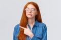 Unsure smart and cute redhead teenager in glasses, female student biting lip curious looking and pointing left, thinking