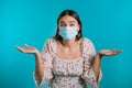 Unsure woman in medical mask shrugs her arms, makes gesture of I don`t know, care, can`t help anything . Girl on blue