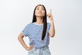 Unsure young asian woman pointing and looking up with troubled, skeptical face expression, having doubts about product Royalty Free Stock Photo